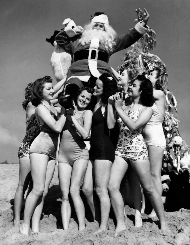 SANTA CLAUS posing surrounded by pretty young things in bathing suits on the beach of Venice, California, on December 4, 1939. In fact, it is Fred ROBERTS, a shoe seller who made a fortune. Dressed as Santa Claus, he shared his wealth by organizing a Christmas party to which hundreds of children were invited. Le PERE NOEL pose entouré de jolies jeunes femmes en maillot de bain, sur la plage de Venice en Californie, le 4 décembre 1939. Il s'agit en fait de Fred ROBERTS, un commerçant en chaussure qui a fait fortune. Celui-ci, déguisé en Père Noël, profite alors de sa fortune en organisant une fête de Noël à laquelle sont conviés des centaines d'enfants.